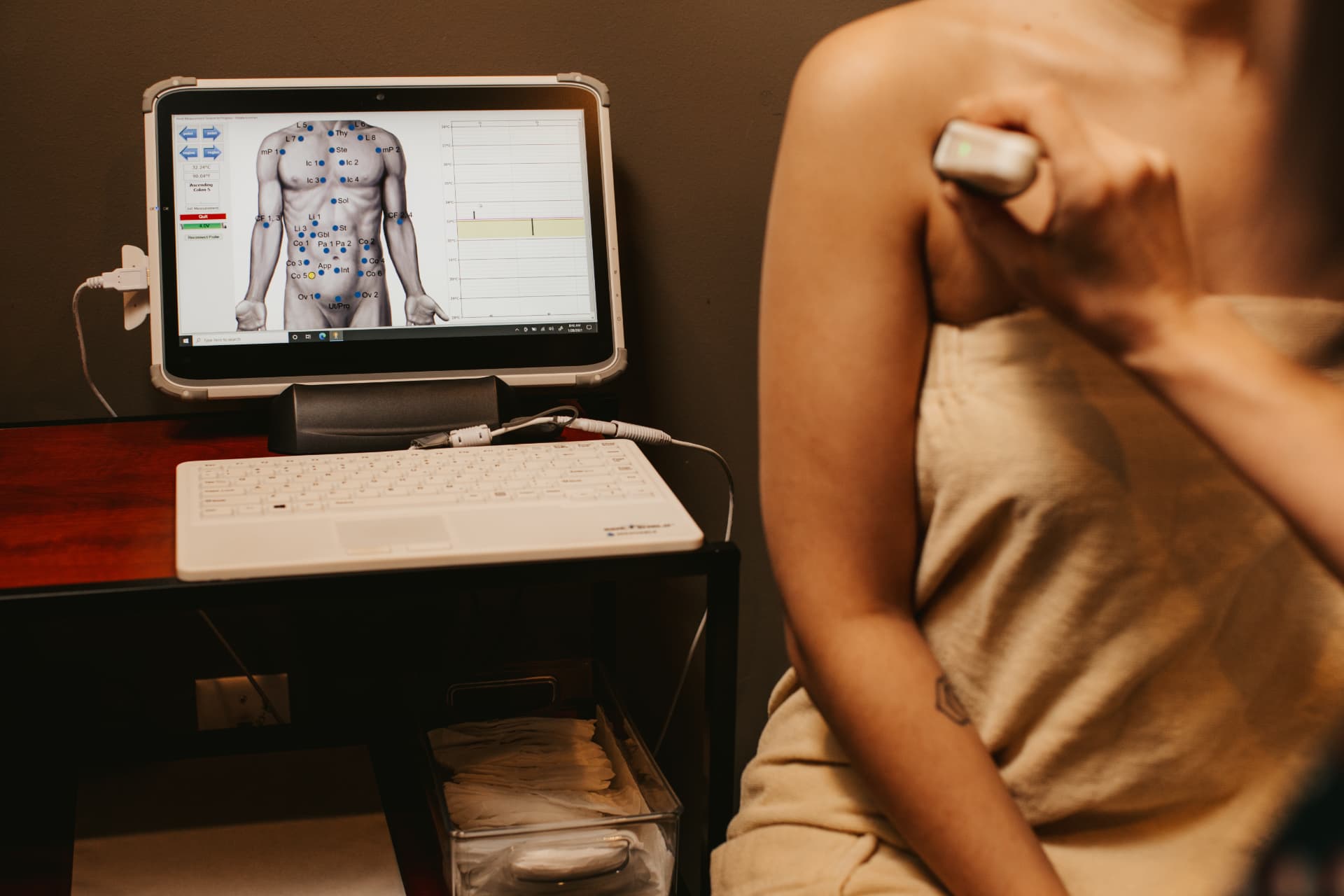 Practitioner running a point-by-point diagnostic scan on a guest's body, results mapped on screen