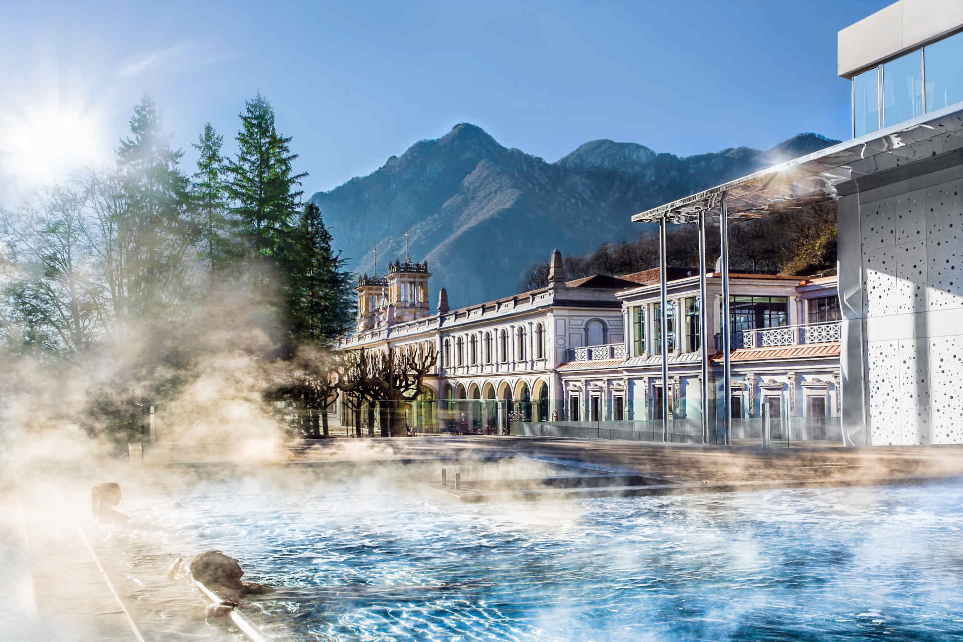 Steaming outdoor thermal pool in front of the historic San Pellegrino spa building and mountains