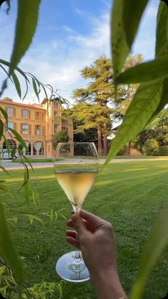 A glass of Franciacorta held up in front of the golden villa at sunset