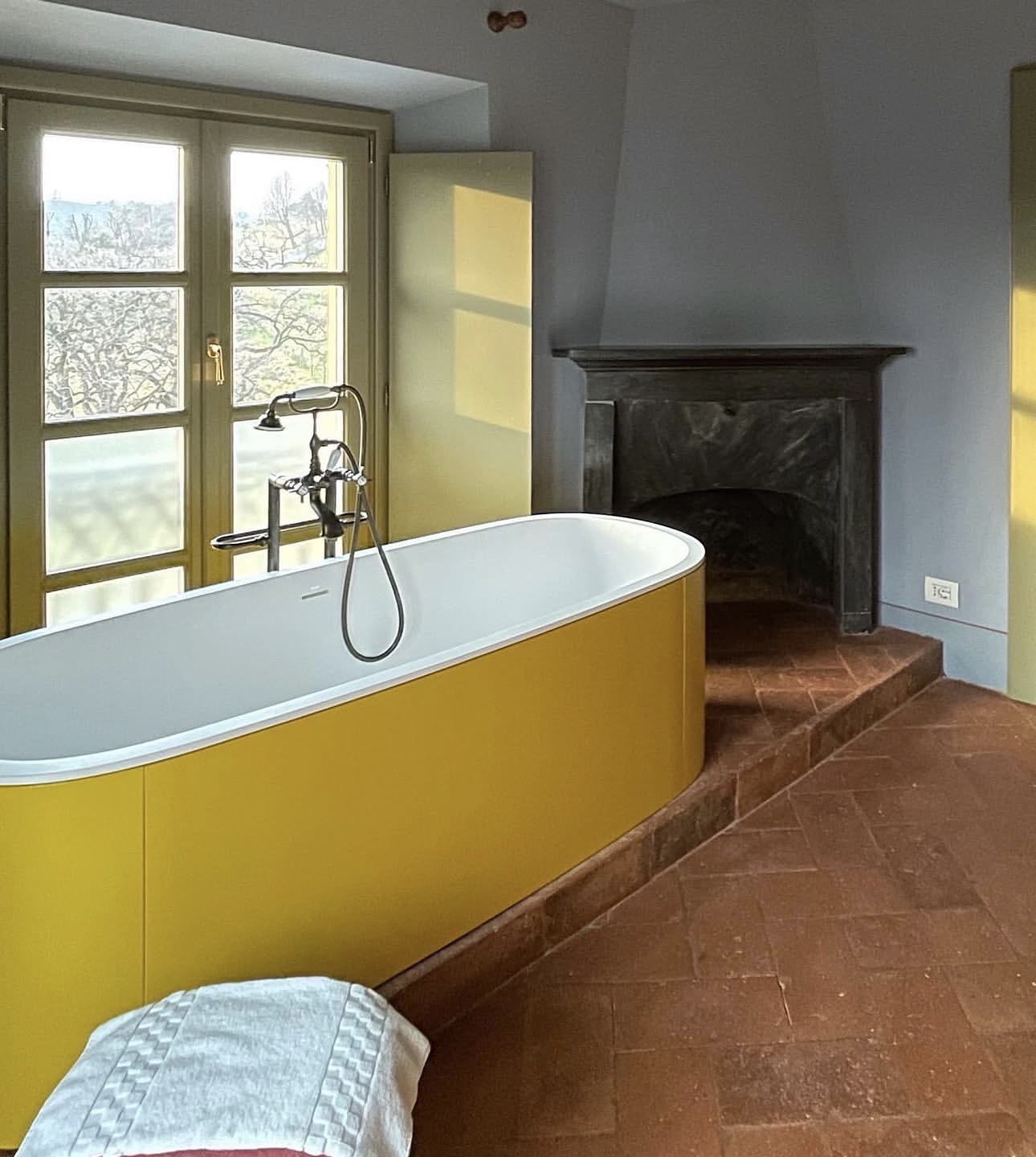 Freestanding ochre soaking tub beside a stone fireplace and terracotta floors