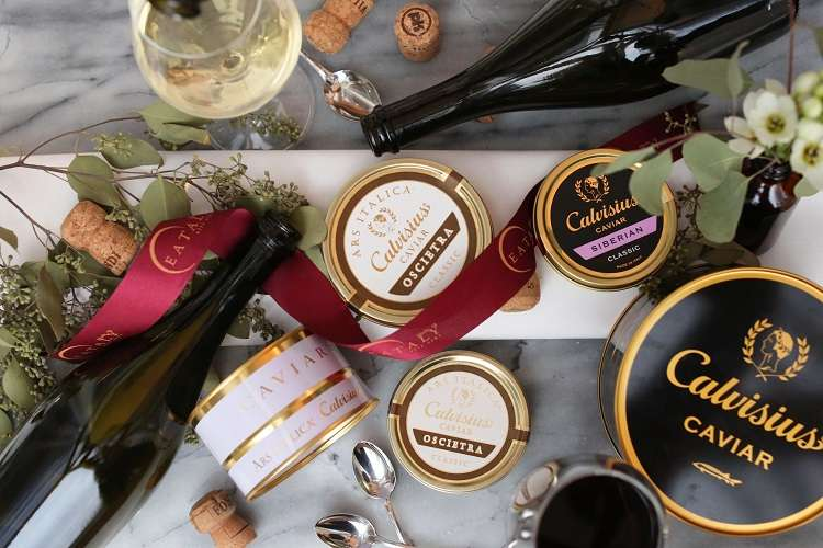 Tins of Calvisius caviar with Franciacorta bottles and glasses on a marble board