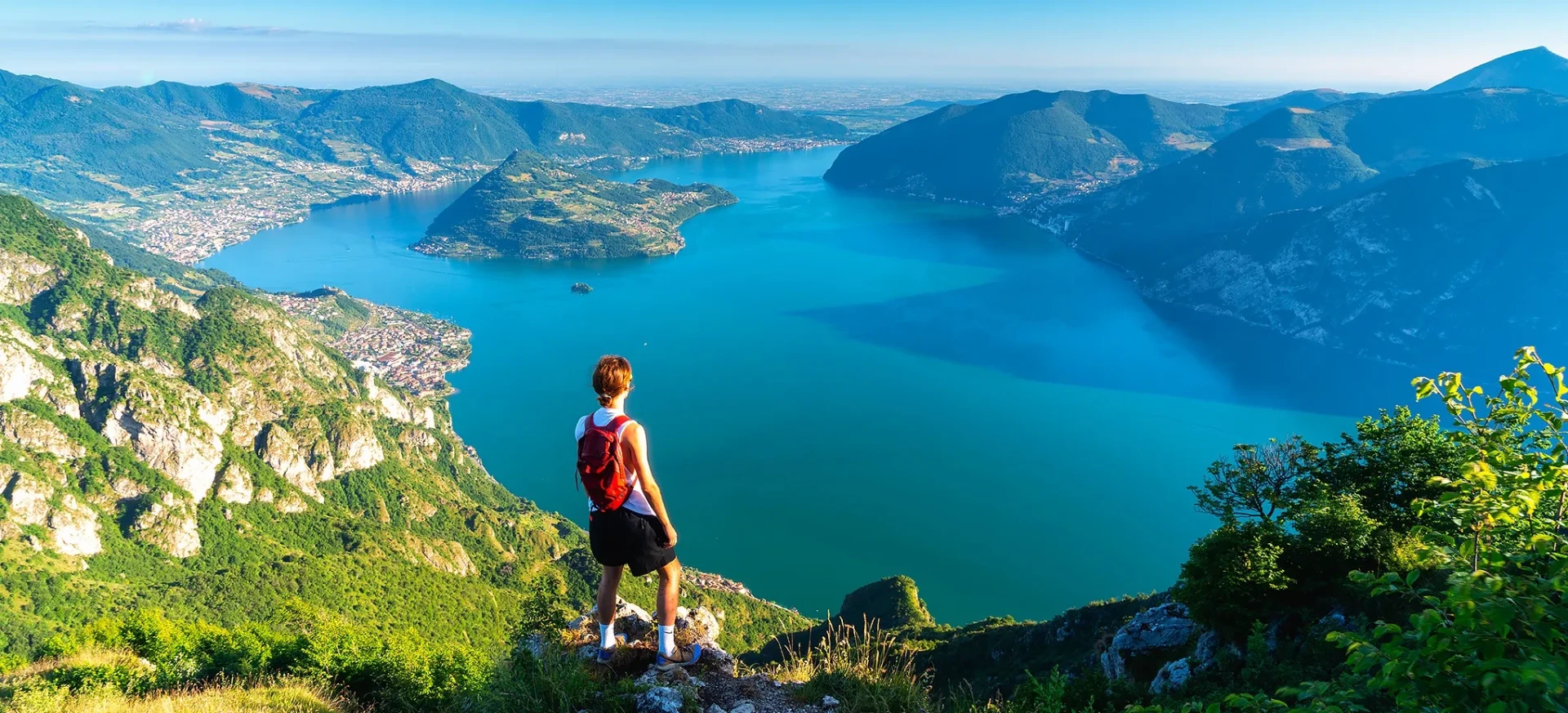 Hiker on a ridge looking down over Lake Iseo and the surrounding mountains
