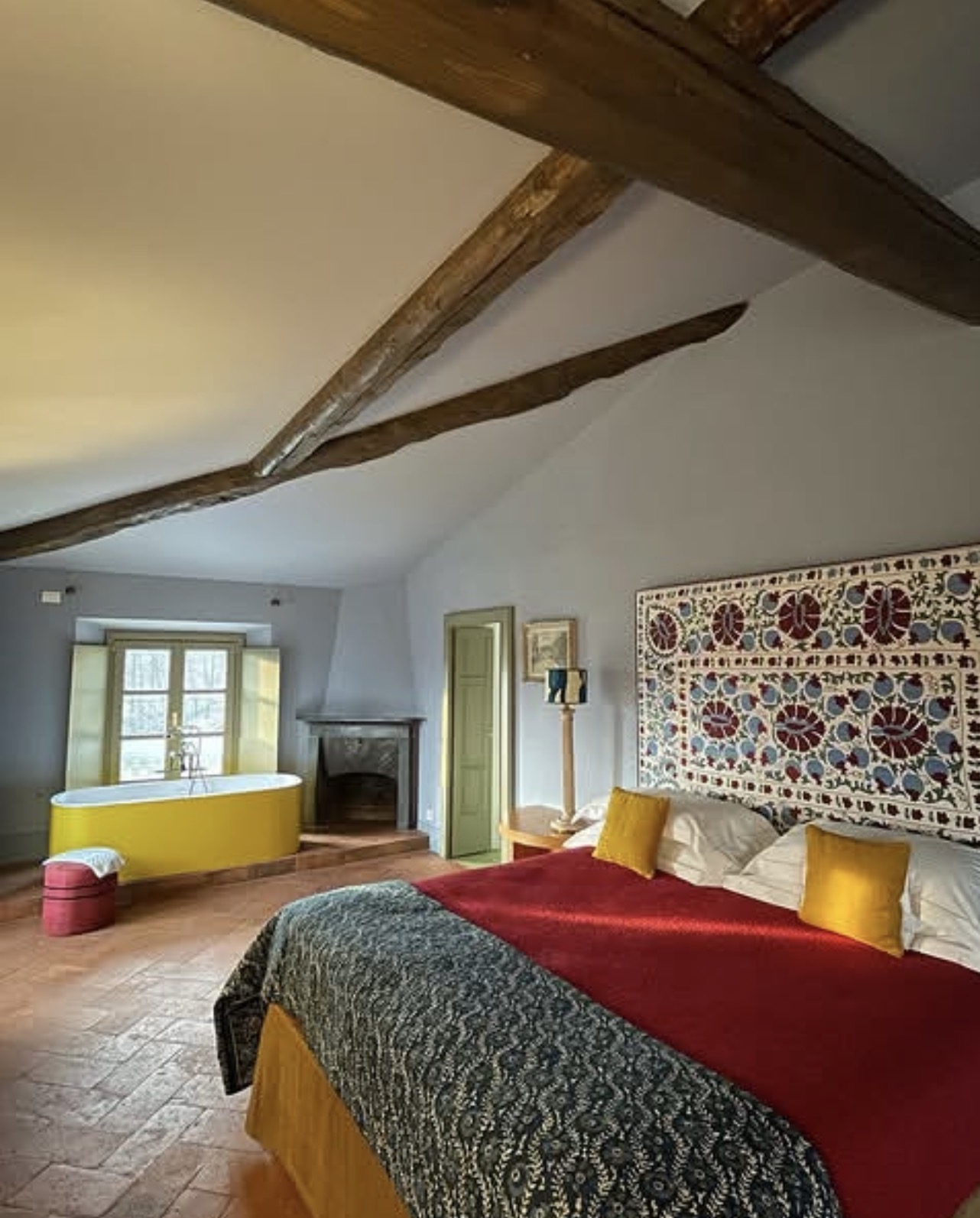 Beamed suite with a yellow freestanding tub, stone fireplace and suzani headboard