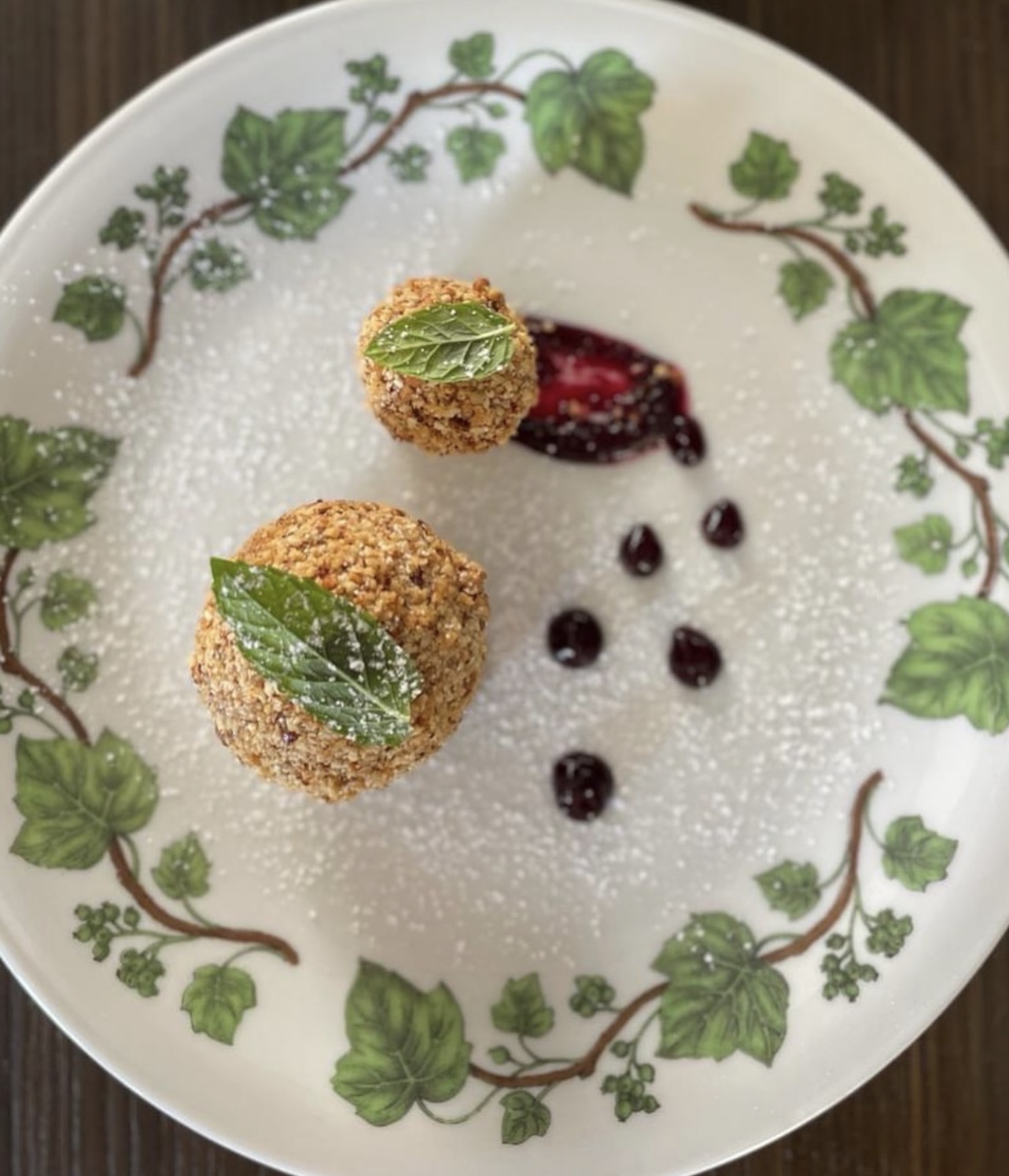 Plated nut-crusted dessert with berry coulis on a vine-patterned plate