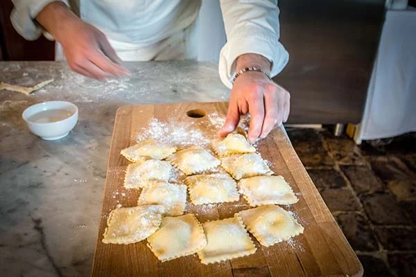 Chef shaping fresh ravioli on a floured wooden board during a cooking class