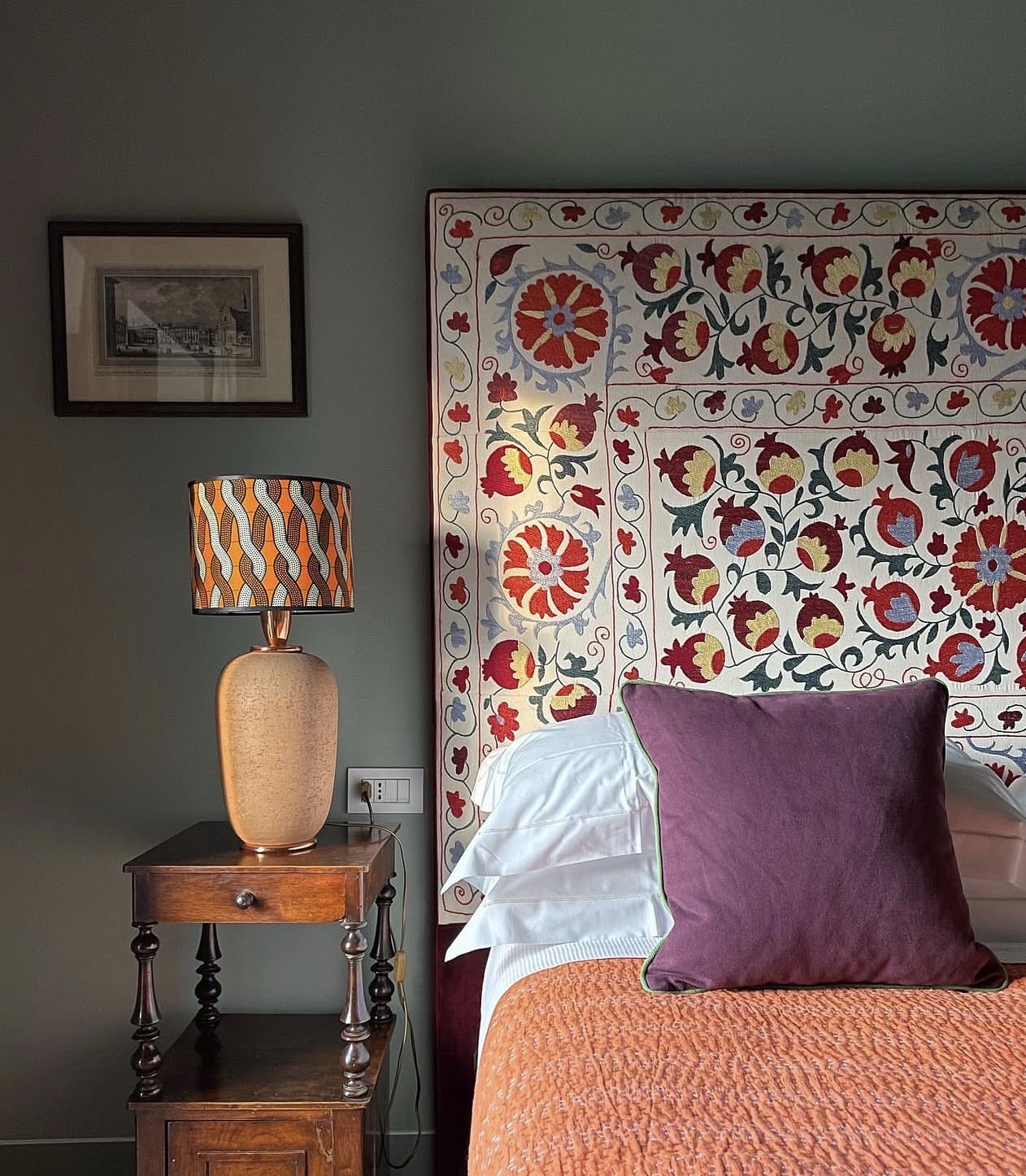 Bedroom with an embroidered suzani headboard, olive walls, and an antique nightstand