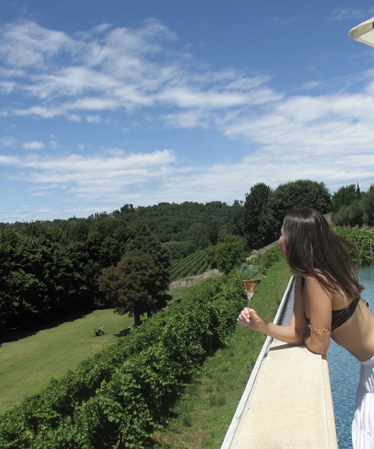 Guest with a glass of Franciacorta looking out over the vineyards from the pool terrace